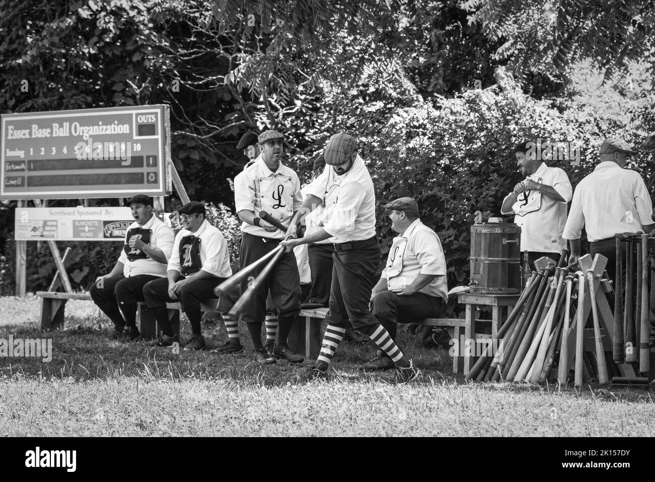 Eine Gruppe von Baseballspielern sitzt auf einer Bank, während ein anderer eine Gruppe von Holzschlägern testet. Vintage-Baseballspiele mit 1860 Regeln, gespielt im Spencer-Pei Stockfoto