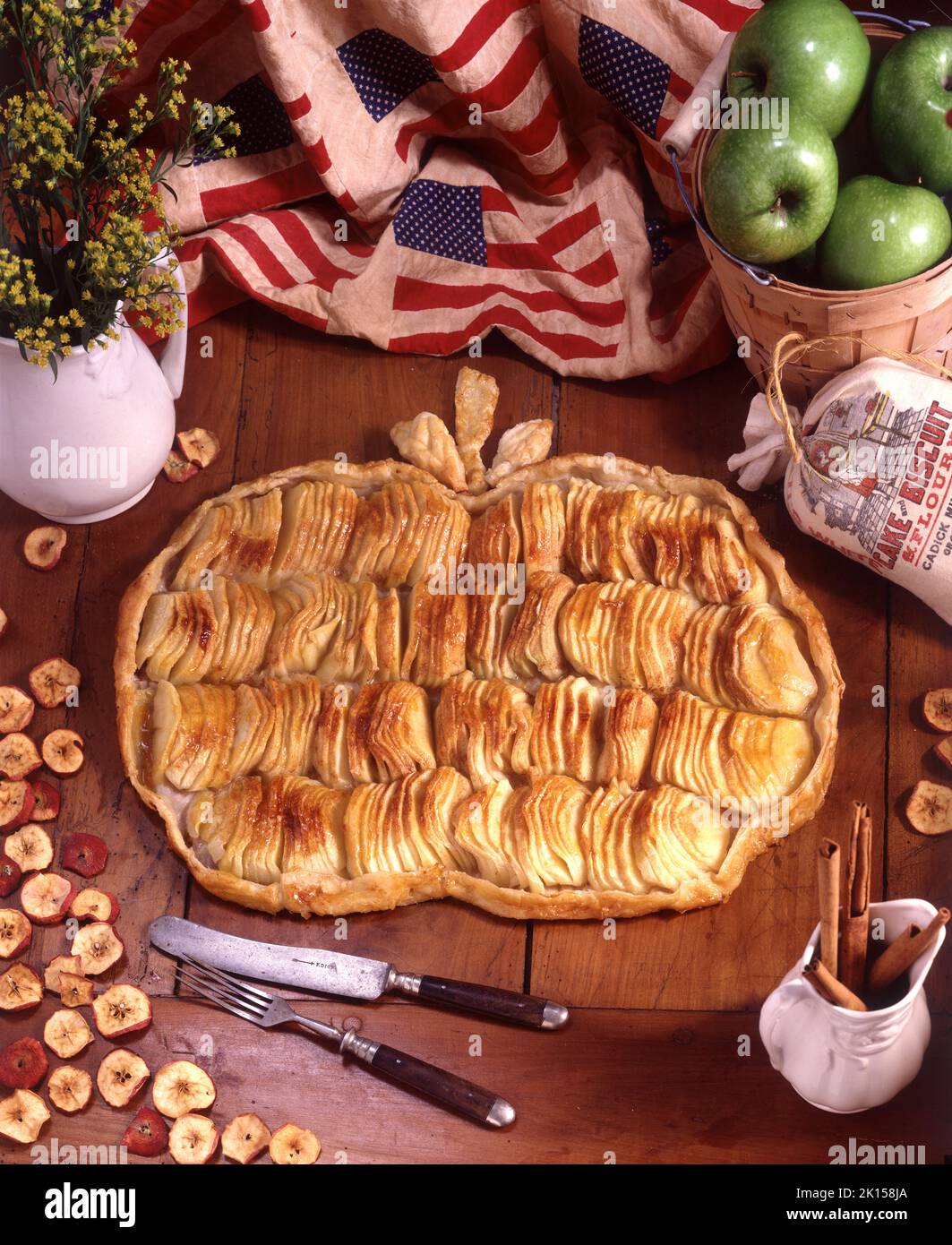 Apfelkuchen in Form eines Apfels. Er befindet sich auf einem antiken Holztisch, umgeben von Requisiten in einem Studiofoto. Stockfoto
