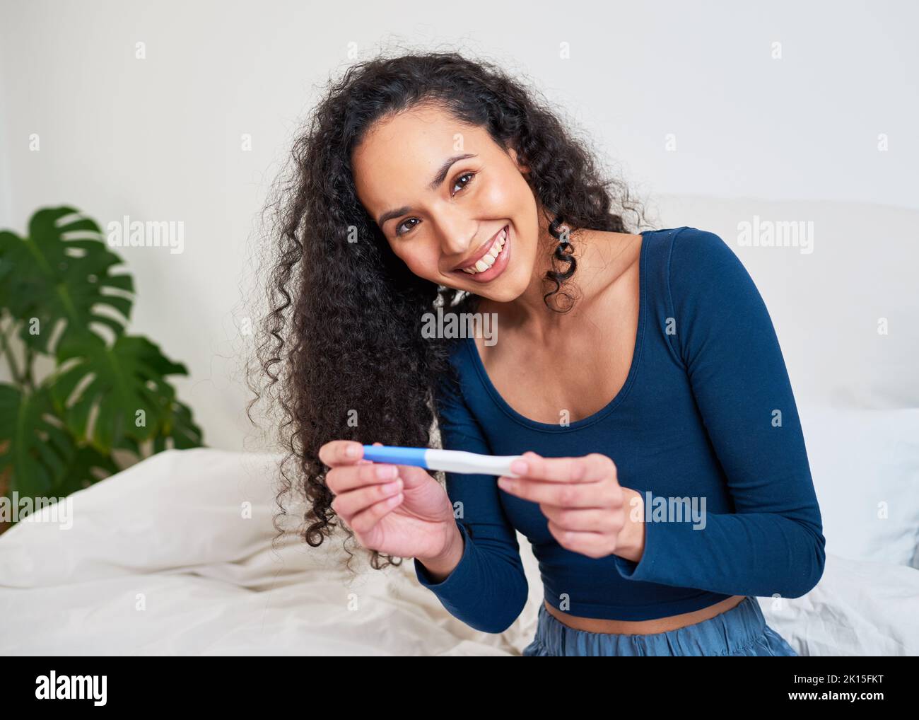 Eine junge, glückliche, multiethnische Frau führt einen Schwangerschaftstest durch und lächelt vor der Kamera Stockfoto
