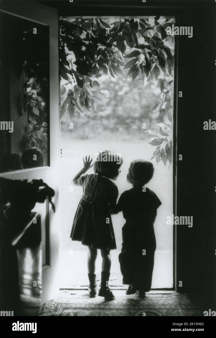 Die Welt draußen. Ein kleiner Junge und ein Mädchen schauen aus der Tür. 50er Jahre. Stockfoto