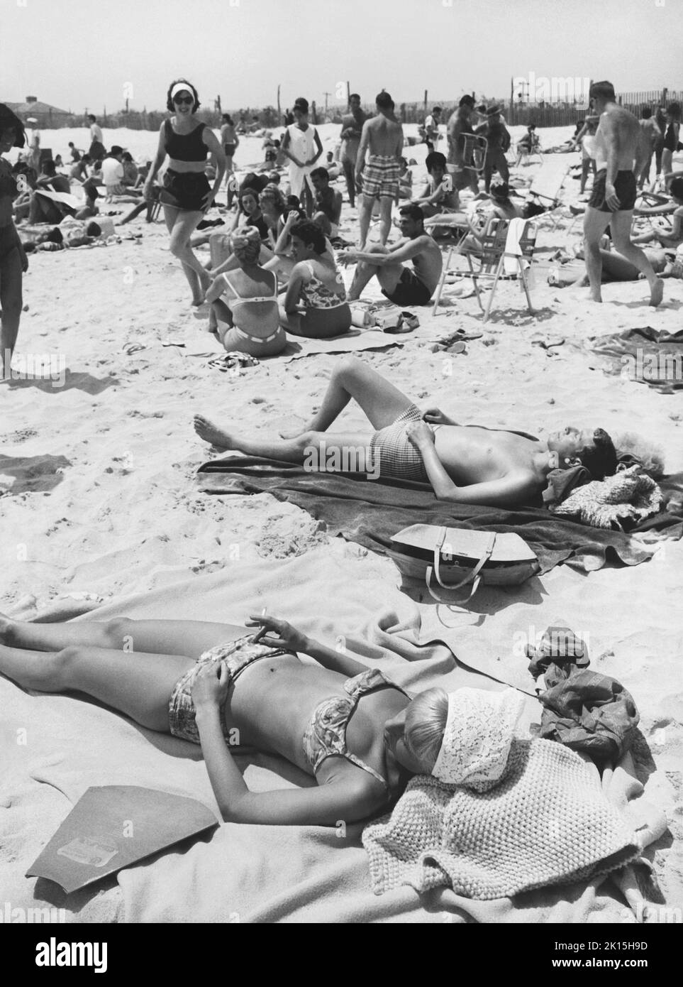 Menschen Sonnenbaden am Strand im Jahr 1963. Beachten Sie den Sonnenreflektor in der linken unteren Ecke des Fotos. Stockfoto