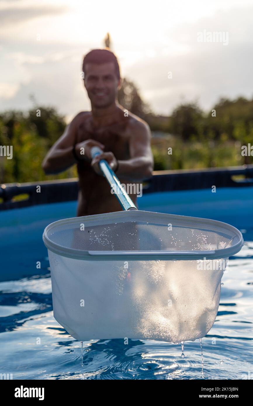 Mann im Pool, der mit Netzgeräten etwas Schmutz vom Wasser entfernt hat Stockfoto