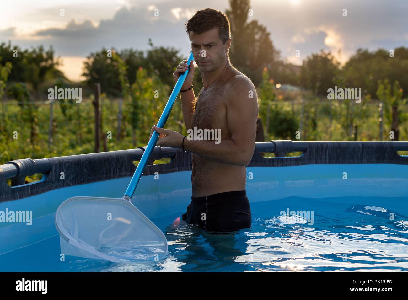 Mann im Pool, der mit Netzgeräten etwas Schmutz vom Wasser entfernt hat Stockfoto