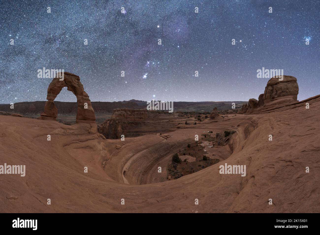Atemberaubende Aussicht auf Delicate Arch in der Nähe des rauen Canyons vor der glühenden Milchstraße am Nachthimmel im Arches National Park in Utah, USA Stockfoto