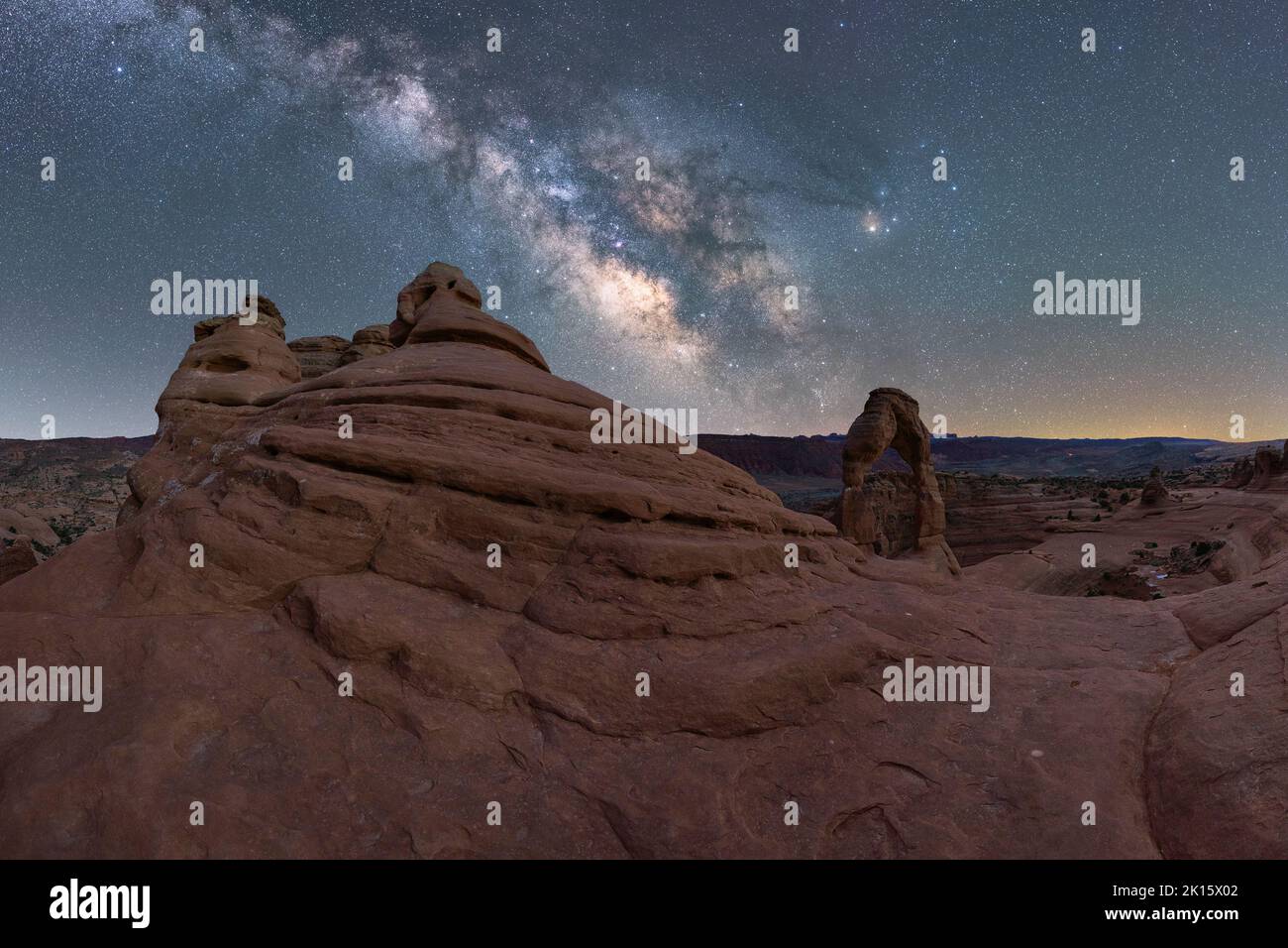 Atemberaubende Aussicht auf Delicate Arch in der Nähe des rauen Canyons vor der glühenden Milchstraße am Nachthimmel im Arches National Park in Utah, USA Stockfoto