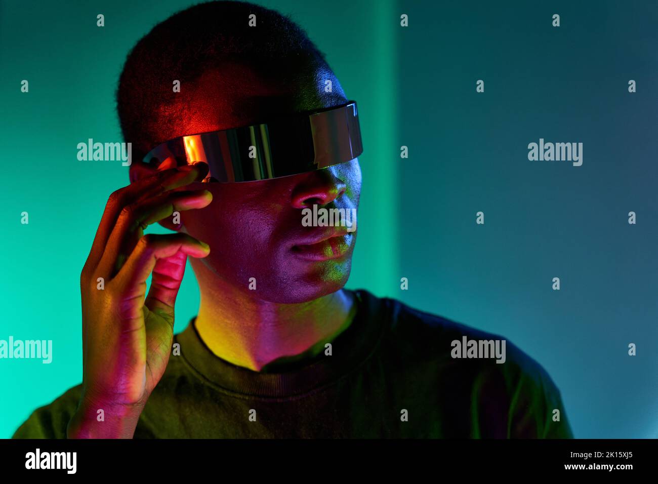 Fokussierter cooler junger Afrikaner in schwarzem T-Shirt, der moderne futuristische Brille anpasst, während er im Studio mit farbenfrohem Ne die virtuelle Realität erlebt Stockfoto