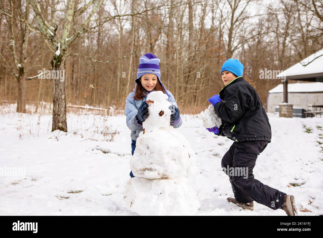 Zwei glückliche Kinder bauen im Winter gemeinsam Schneemann Stockfoto