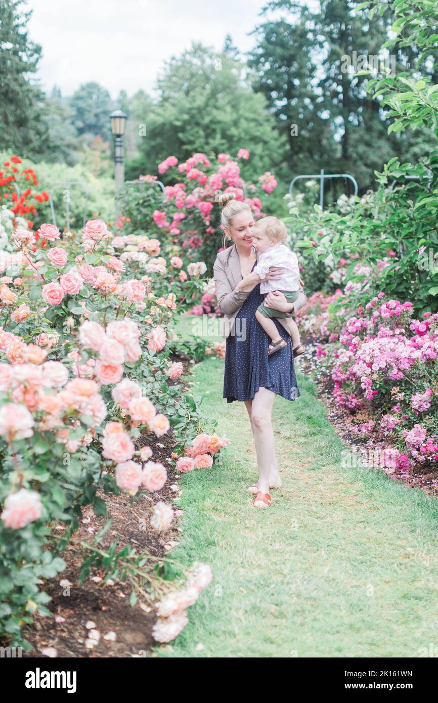 Kaukasische 30-jährige Mutter hält Kleinkind Sohn im Rosengarten. Stockfoto