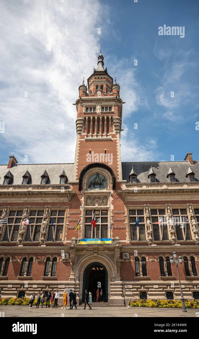 Europa, Frankreich, Dunkerque - 9. Juli 2022: Menschen vor dem Glockenturm des historischen Rathauses unter blauer Wolkenlandschaft. Flaggen, Statuen und Ukraine Soli Stockfoto