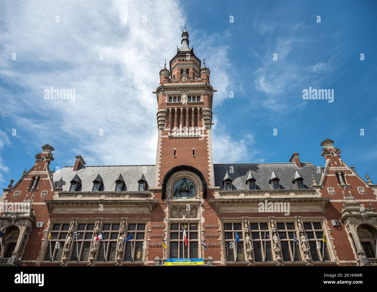 Europa, Frankreich, Dunkerque - 9. Juli 2022: Nahaufnahme des Belfry-Turms und der obersten Ebene des historischen Rathauses unter blauer Wolkenlandschaft. Flaggen, Statuen und Ukrain Stockfoto