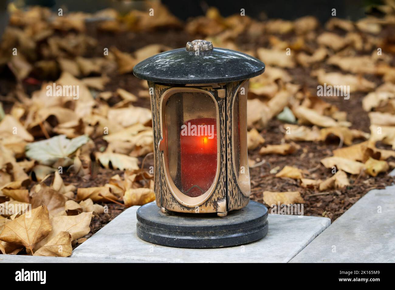 gedenklaterne mit brennender Kerze auf einem Grab mit Herbstblättern Stockfoto