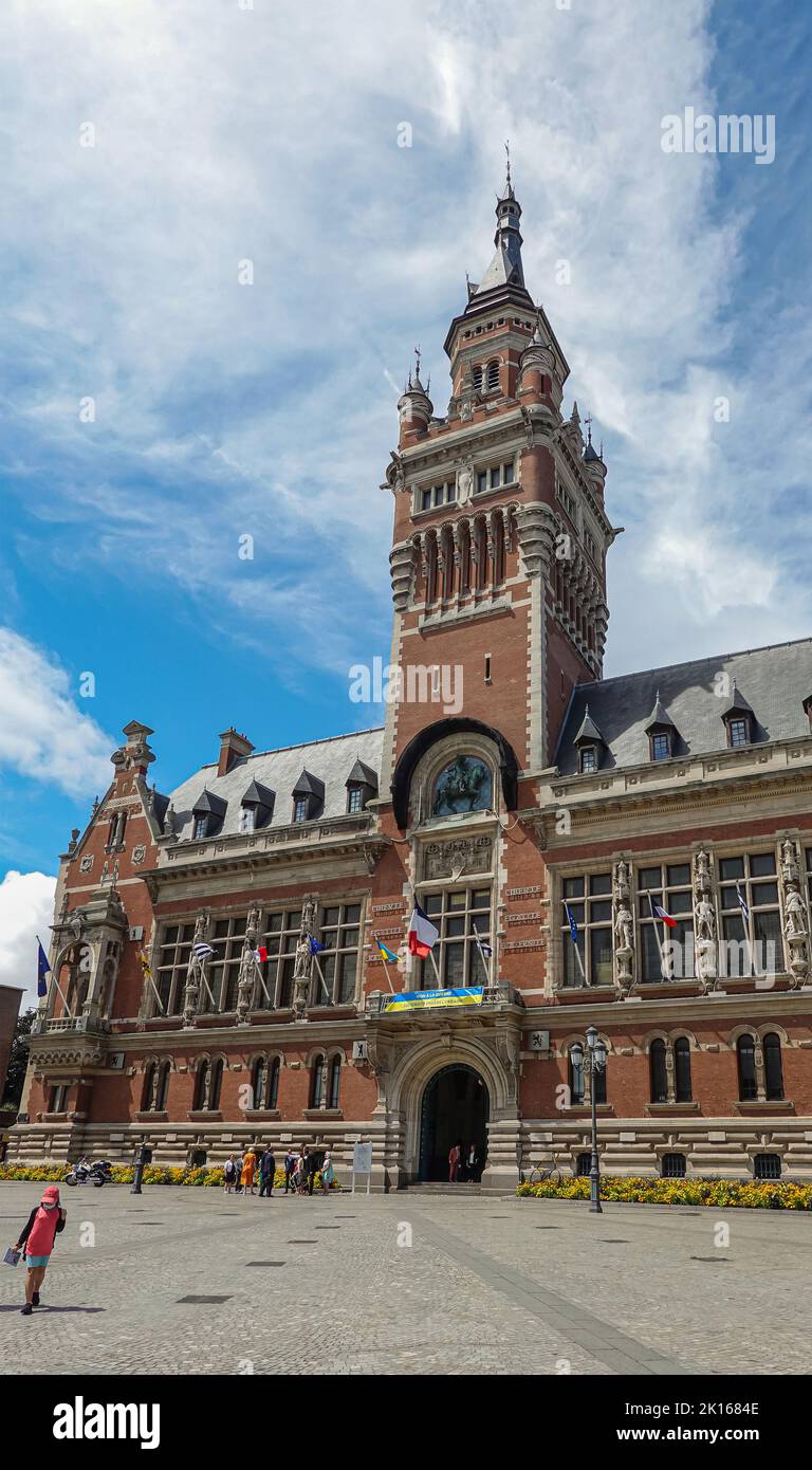 Europa, Frankreich, Dunkerque - 9. Juli 2022: Menschen auf dem Platz Charles Valentin vor dem Glockenturm des historischen Rathauses unter blauer Wolkenlandschaft. Alarmmeldung Stockfoto