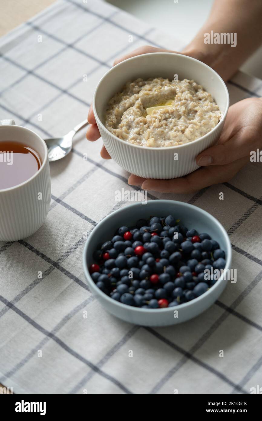 Gesundes Essen Frühstück mit Haferbrei Haferbrei in einer Schüssel mit Sommerbeeren, Butterscheibe, Tasse Tee. Stockfoto
