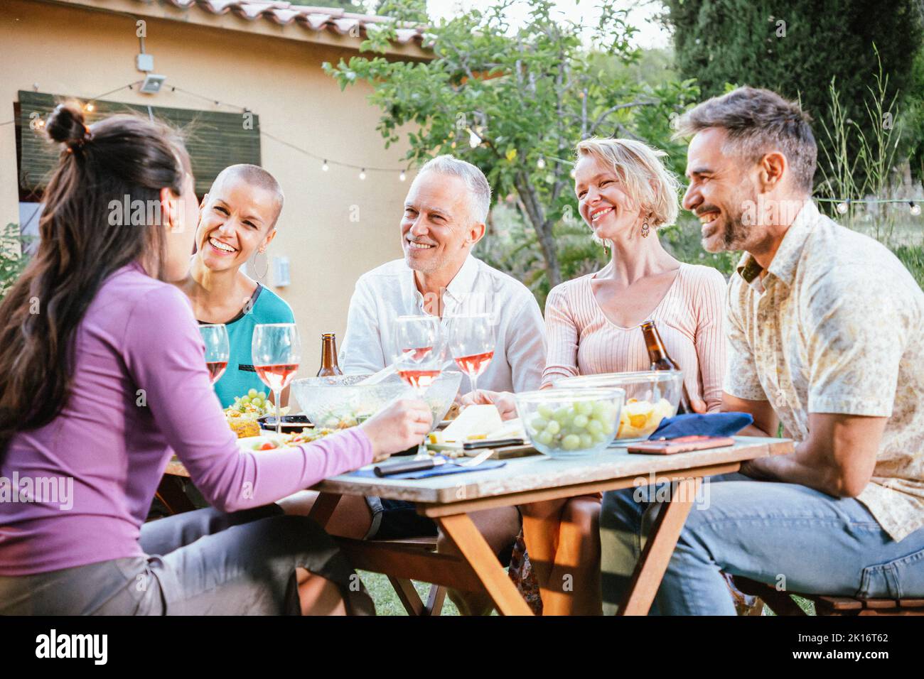 Eine Gruppe von erwachsenen Freunden, die seine Weingläser und Biere toasten und sich auf einer Dinnerparty im Hinterhof amüsieren. Lifestyle-Konzept. Stockfoto