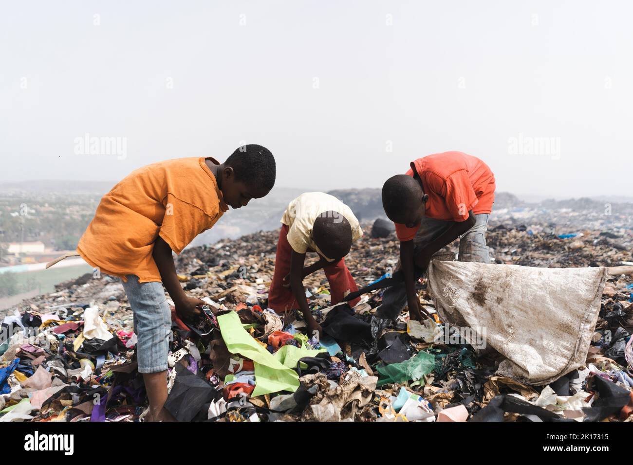 Gruppe obdachloser Straßenkinder, die in einer dampfenden Deponie in einer afrikanischen Metropole Müll sammeln; Konzept von Armut und Vernachlässigung von Kindern Stockfoto