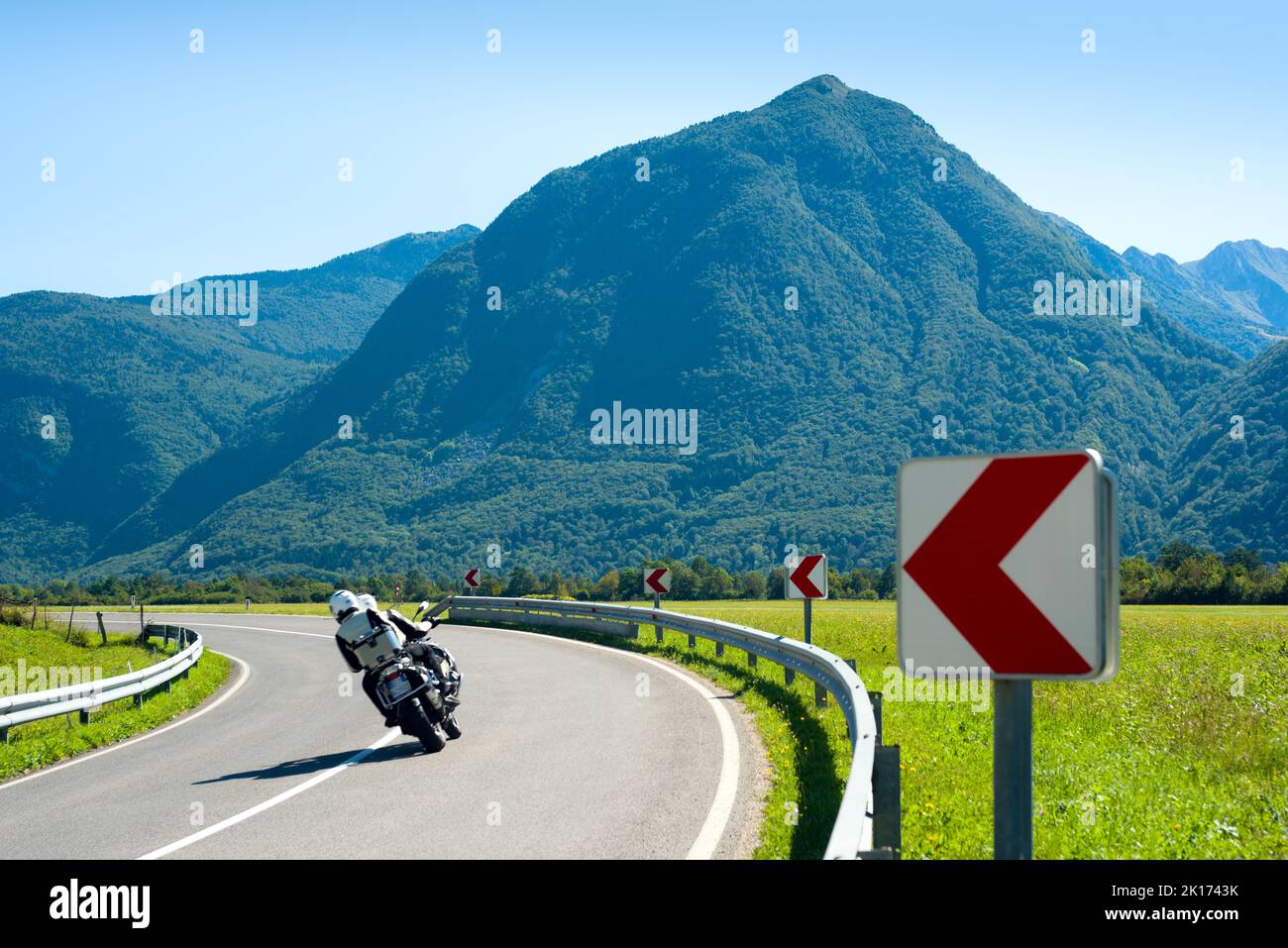 Motorrad, das an einer Abbiegung auf der alpinen Autobahn gegen den blauen Berg vorbeifährt Stockfoto