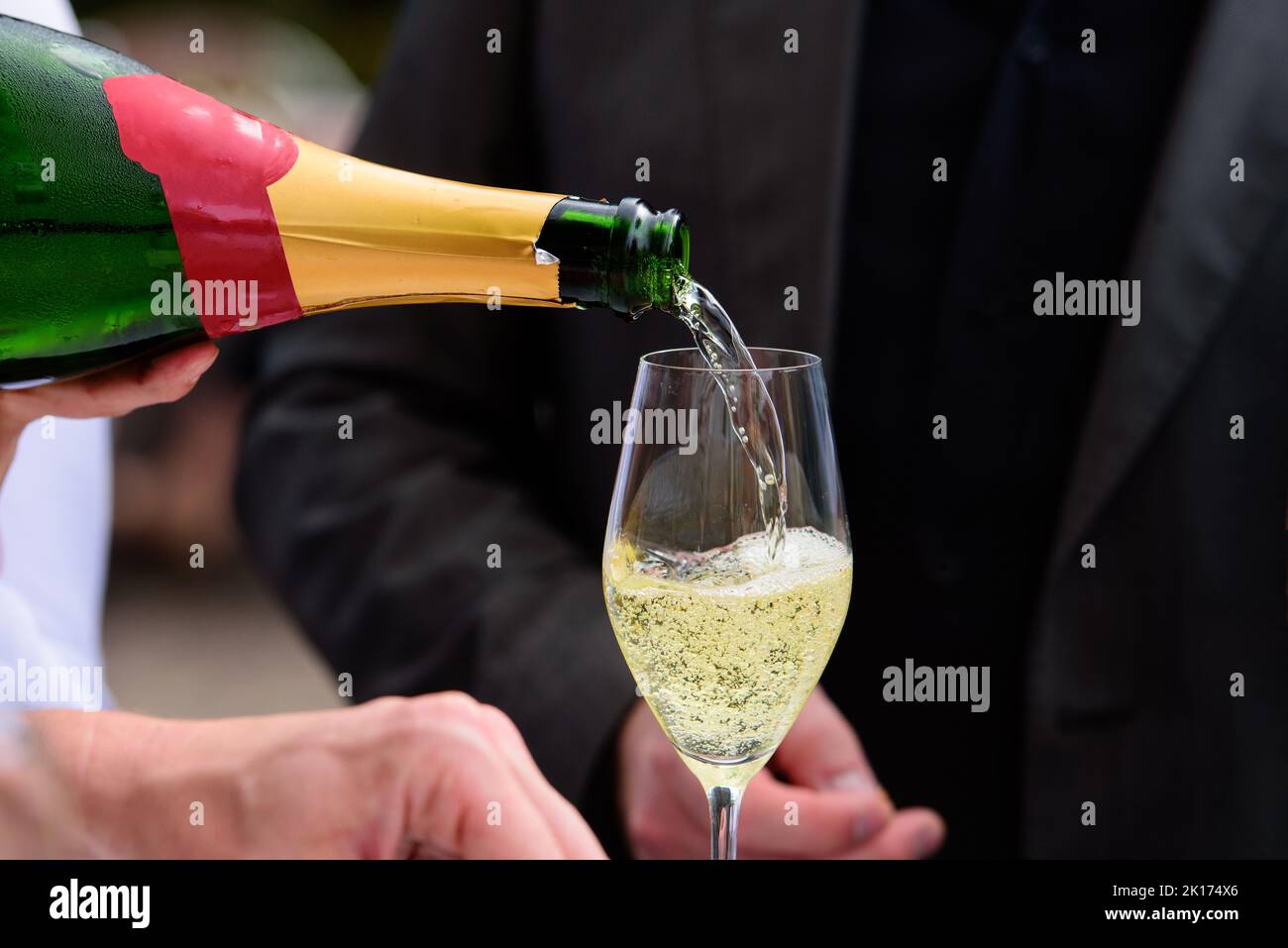 Nahaufnahme einer Champagnerflasche, die Champagner auf einer Sektflöte gegen eine verschwommene Person auf einer Party umschaufelt Stockfoto