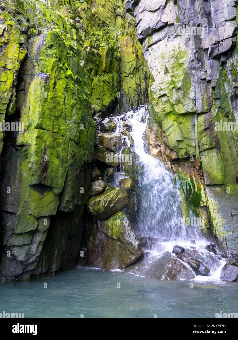 Spektakuläre Aussicht auf einen Wasserfall auf einem Gletscher. Die Vogelklippe Alkefjellet ist die berühmteste Klippe des Spitzbergen-Archipels. Hinloopen Fjord, Spitzbergen. Stockfoto