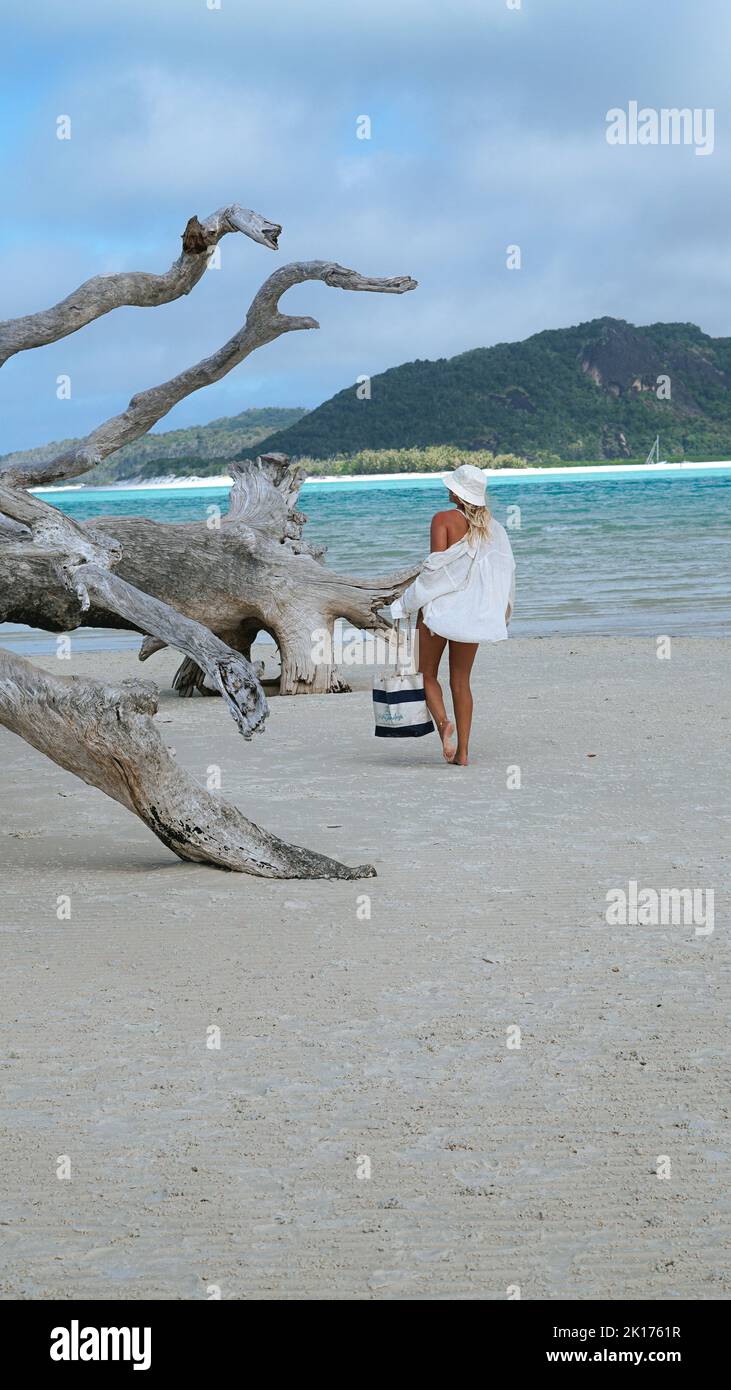 Frau in einem Eimerhut und einem weißen Hemd mit einer Tragetasche beim Spaziergang neben dem berühmten Baum am Whitehaven Beach in den Whitsundays, Australien. Stockfoto