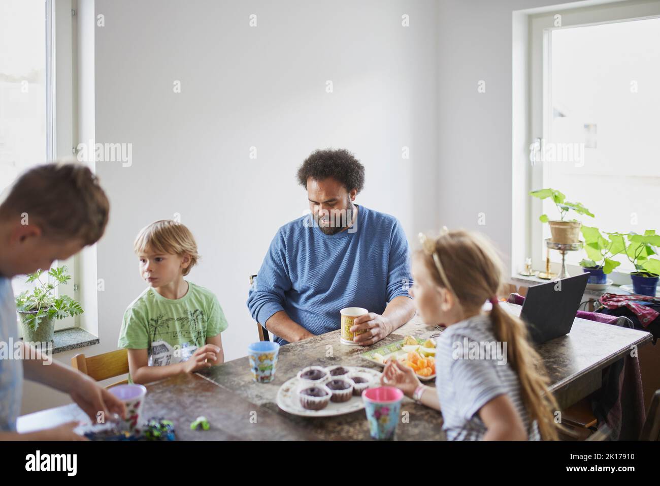 Vater mit Kindern, die am Tisch sitzen und einen Snack essen Stockfoto