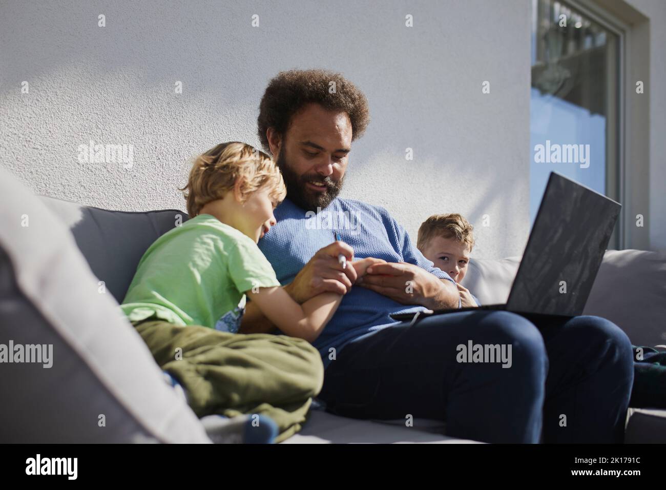 Vater sitzt mit Söhnen auf Deck und arbeitet an einem Laptop Stockfoto