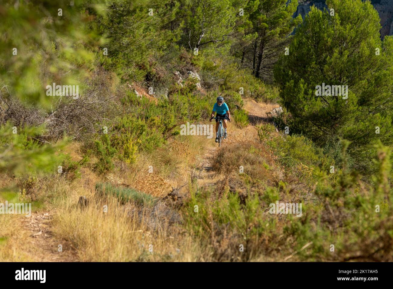 Ein männlicher Radfahrer in einer mediterranen Wald Schotterstraße Fahrradtour in der Costa Blanca, Alicante, Spanien Stockfoto