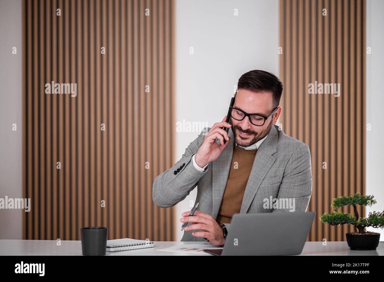 Ruhiger Büroangestellter, der mit seinem Firmenjubelmann am Telefon spricht, während er mit seinem Stift herumzackelt. Stockfoto