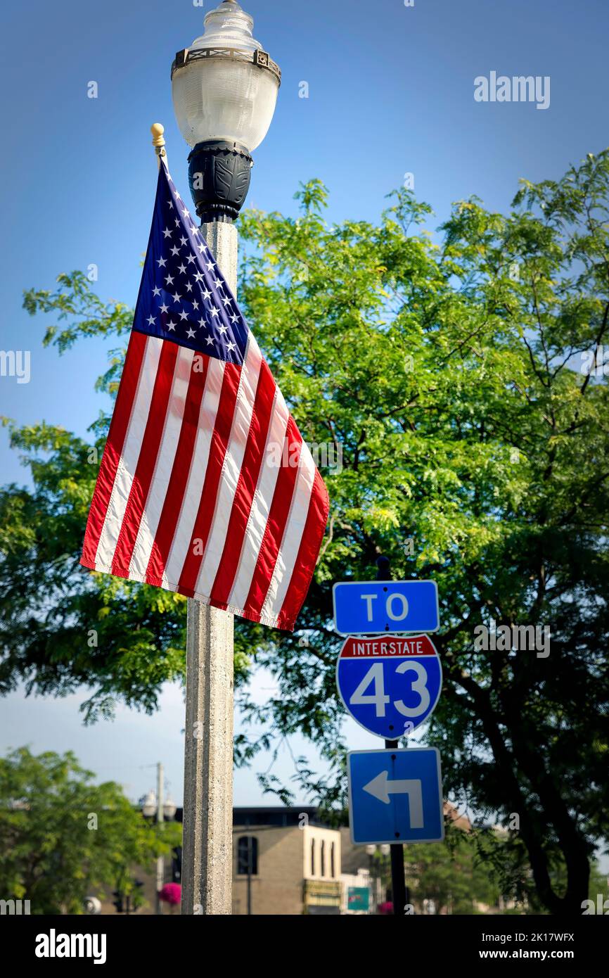 Eine amerikanische Flagge auf einem Lichtpfosten steht neben einem Straßenschild zur I-43 in Two Runs, Wisconsin. Stockfoto