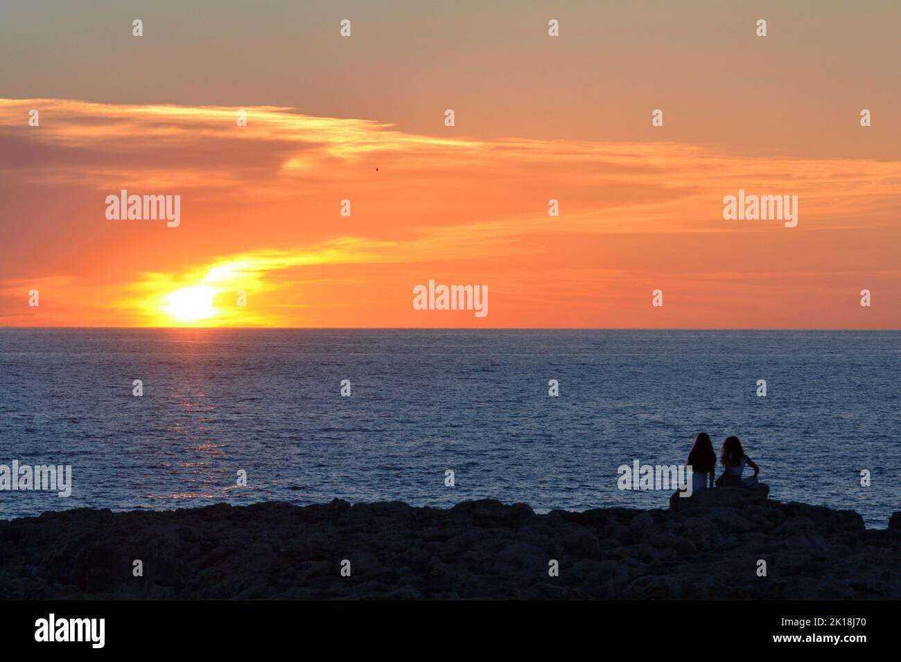 Sonnenuntergang in Cala Blanca, in der Nähe von Cuitadella, Menorca, mit Paaren, die gegen den Himmel geschildet sind Stockfoto