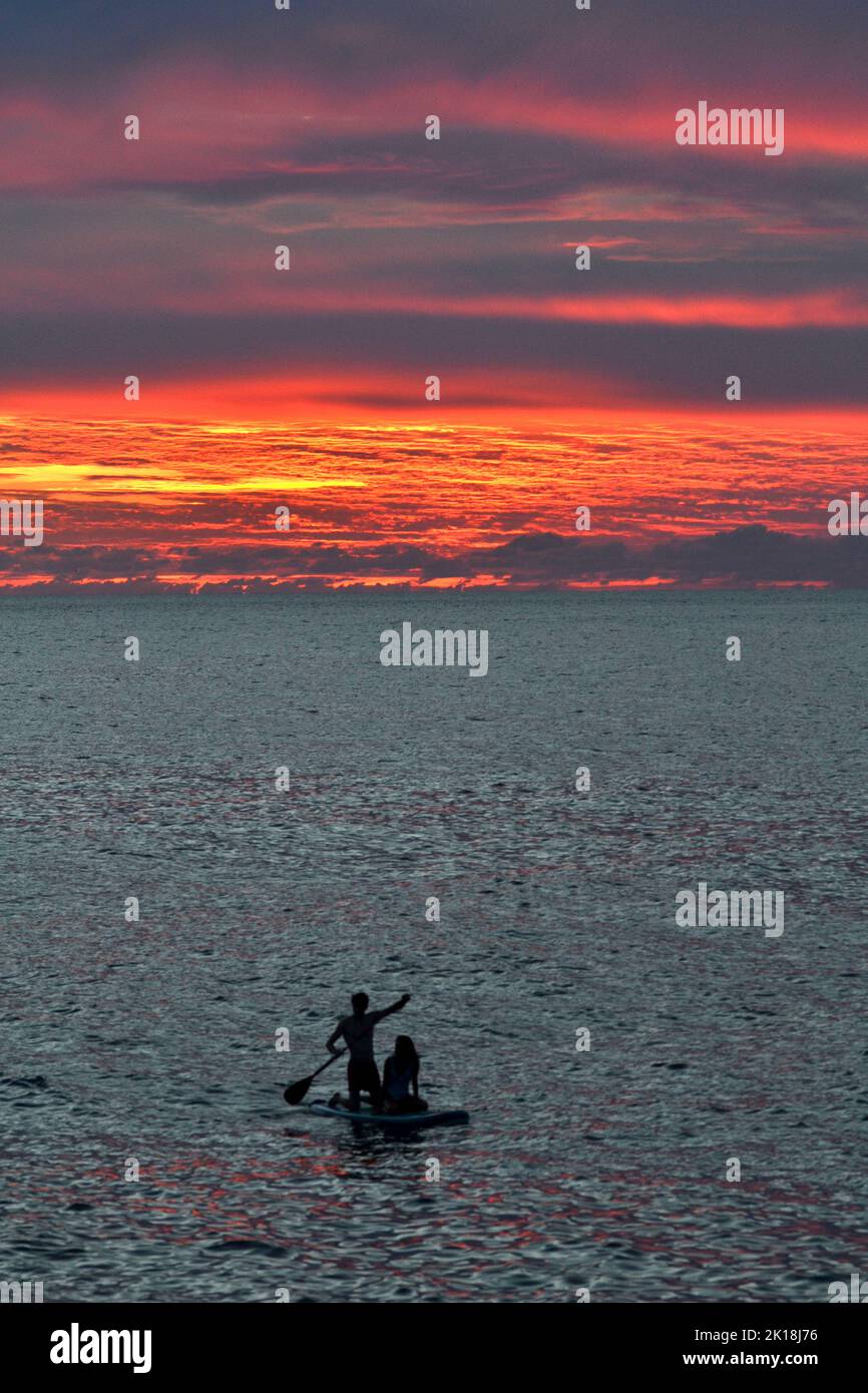 Sonnenuntergang in Cala Blanca, in der Nähe von Cuitadella, Menorca, mit einem Paar auf einem Stand-up-Paddleboard Stockfoto