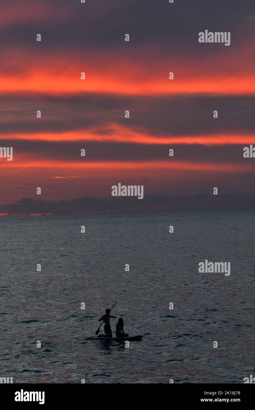 Sonnenuntergang in Cala Blanca, in der Nähe von Cuitadella, Menorca, mit einem Paar auf einem Stand-up-Paddleboard Stockfoto