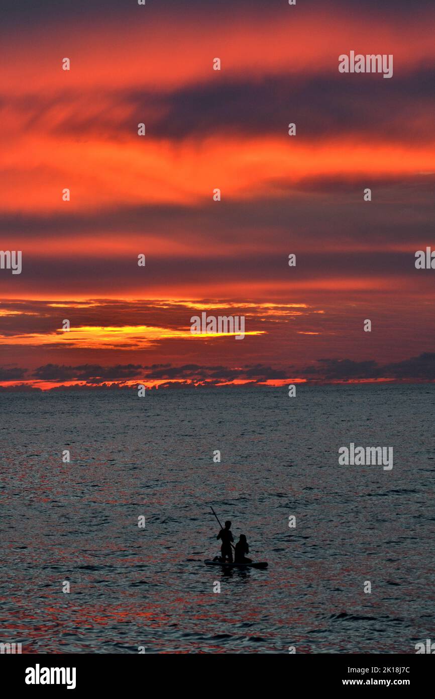 Sonnenuntergang in Cala Blanca, in der Nähe von Cuitadella, Menorca, mit einem Paar auf einem Stand-up-Paddleboard Stockfoto