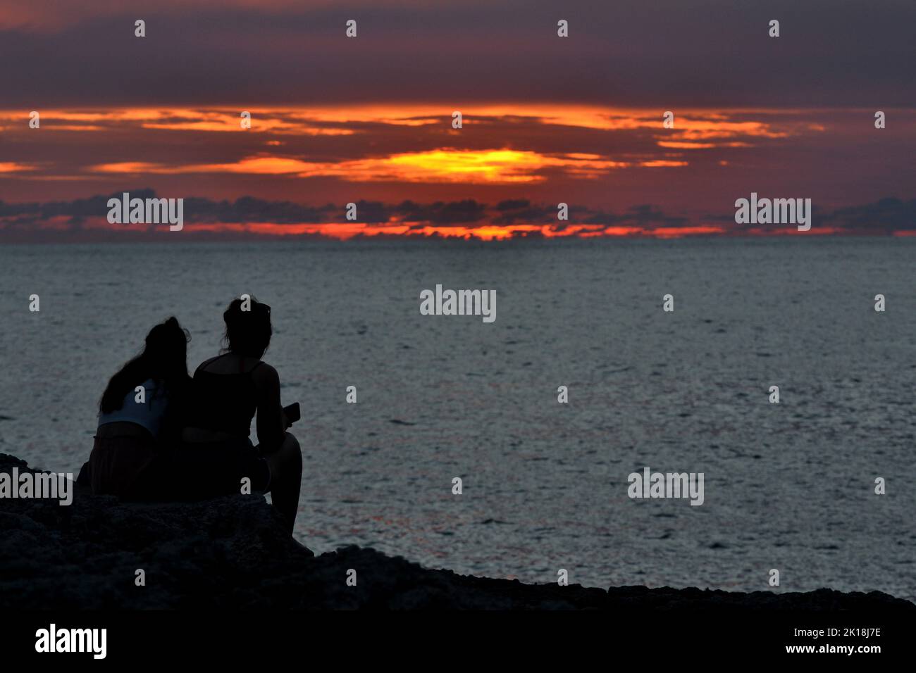 Sonnenuntergang in Cala Blanca, in der Nähe von Cuitadella, Menorca, mit Paaren, die gegen den Himmel geschildet sind Stockfoto