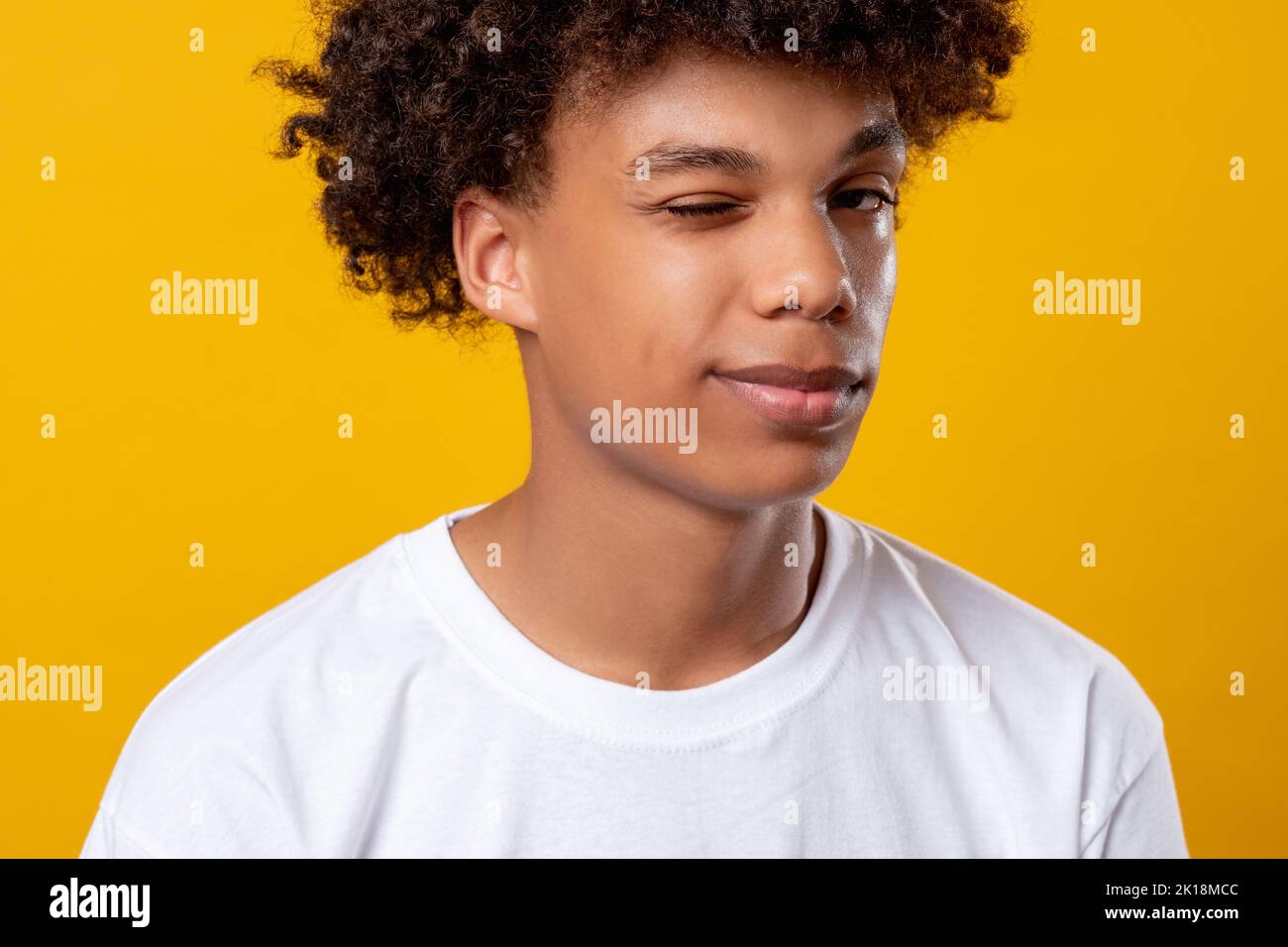 Schwarzes Teenager-Porträt. Positive Stimmung. Lächelnder afrikanischer Student, der die Kamera blinzelnd ansieht. Auf orangefarbenem Kopierbereich isoliert. Ethnische Toleranz. Konfi Stockfoto
