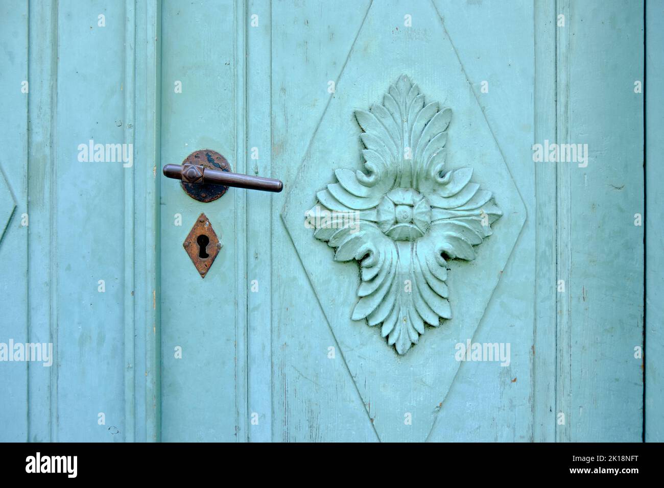 Alte Vintage-Türbeschläge auf einer grünen Tür mit verzierten Kassettenplatten. Stockfoto