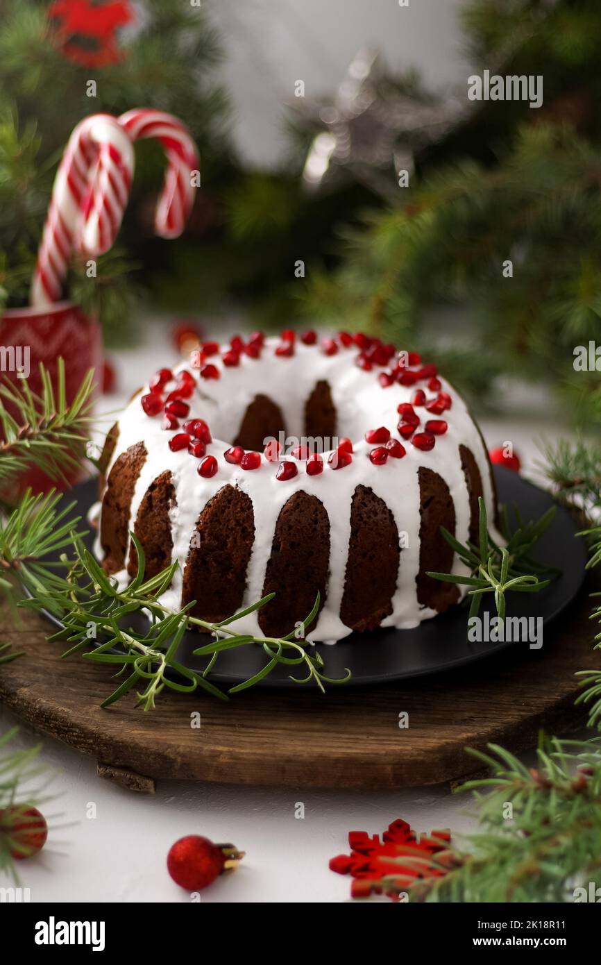 Weihnachtliches Essen. Runde Torte mit weißer Glasur. Cupcake mit einem Loch in der Mitte mit Granatapfel. Grüne Fichtenzweige auf dem Tisch. Stillleben. Süßes Gebäck, Desserts und Leckereien für das neue Jahr. Stockfoto