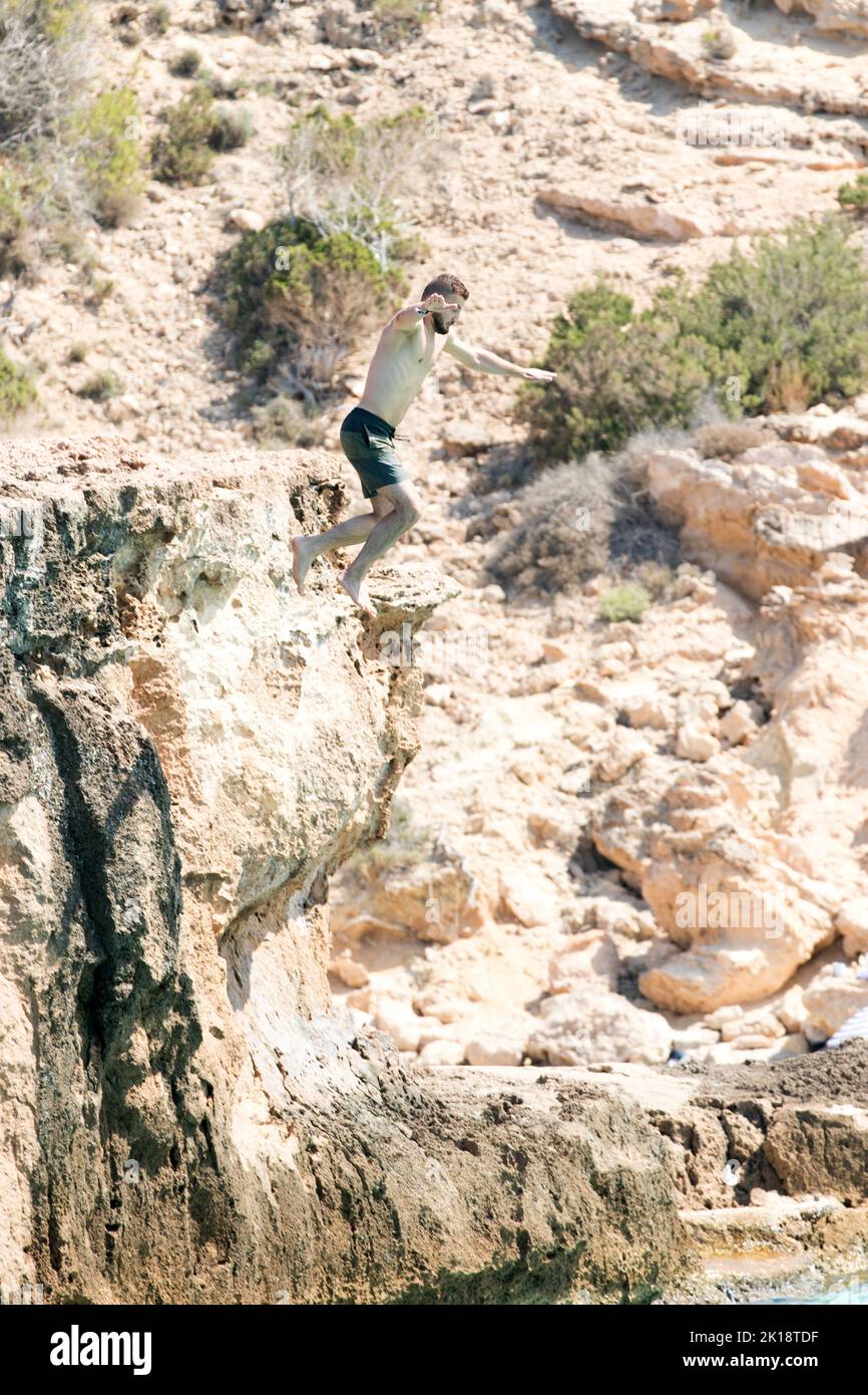 Urlauber auf der Insel Ibiza genießen es, von einem Felsen ins Meer zu springen. Die Insel hat viele tiefe Buchten und felsige Aufschlüsse. Stockfoto