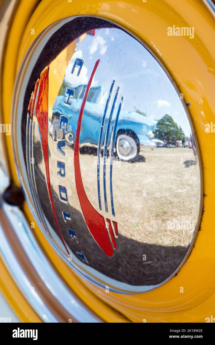 Spiegelungen eines Oldtimer in der glänzend polierten Chrom-Nabenkappe eines Chevrolet-Rades auf der Classic Car Show in Saffron Walden, Essex, Großbritannien Stockfoto