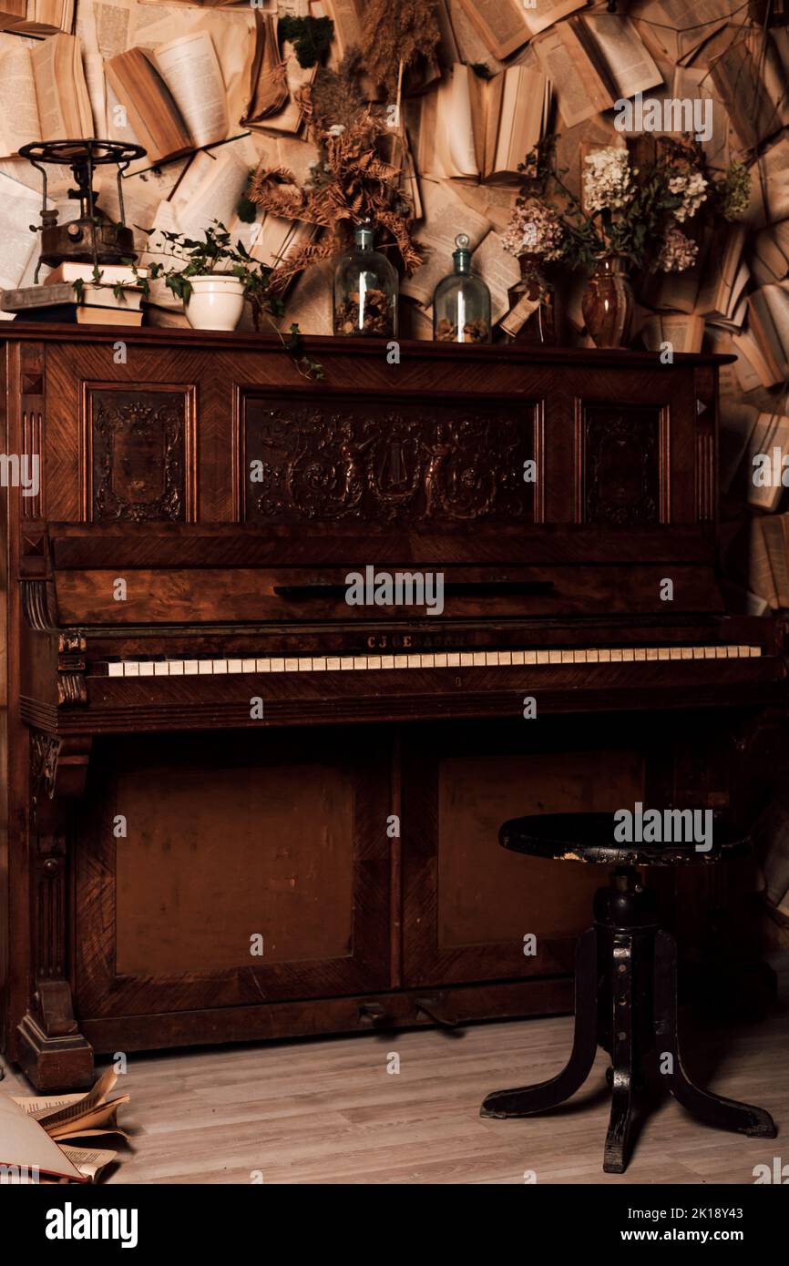 Ein altes Klavier in einem dunklen Raum. Viele Bücher an den Wänden Stockfoto