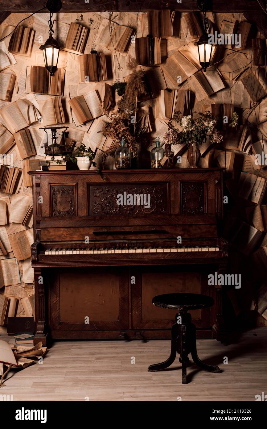 Ein altes Klavier in einem dunklen Raum. Viele Bücher an den Wänden Stockfoto