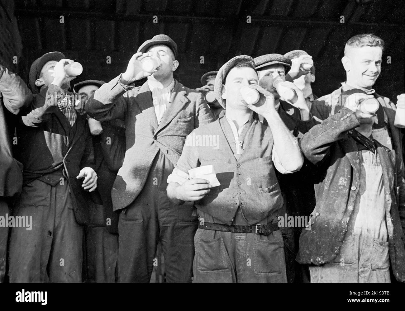 1937, historisch, Arbeitspause....eine Gruppe von Mühlenarbeitern trinkt Flaschen Milch draußen in einem Arbeitshof bei der British Coated Board & Paper Mills Ltd, Treforest Trading Estate in South Wales, Großbritannien. Stockfoto