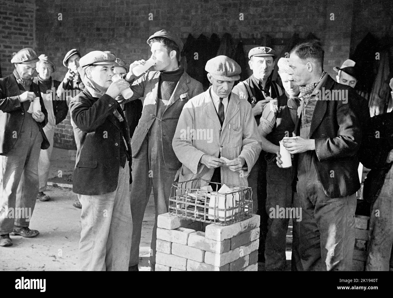1930er Jahre, historisch, Arbeitspause....Sägearbeiter trinken Flaschen Milch in einem Außenhof der British Coated Board & Paper Mills Ltd, Treforest Trading Estate, South Wales, UK. Die Mühle war die erste Fabrik, die auf dem Handelsgut gebaut wurde, ursprünglich bekannt als „South Wales and Monmouthshire Trading Estate’s Ltd“, ein gemeinnütziges Unternehmen, das gegründet wurde, um Handelsgüter zu errichten und Arbeitsplätze in Wales zu schaffen. Stockfoto