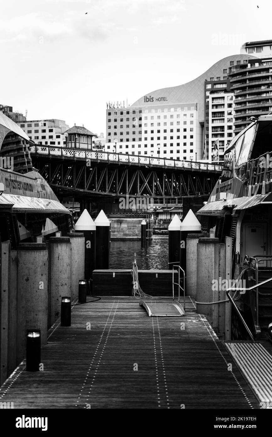 Eine vertikale Graustufenansicht eines Hafens und architektonischer Gebäude im Hintergrund in Sydney, Australien Stockfoto