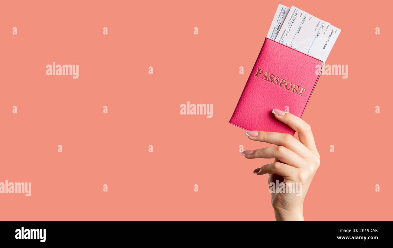 Passkontrolle. Globale Einwanderung. Weibliche Hand, die einen ausländischen ausweis in pinkfarbenem Cover hält, ein First Class-Flugticket, das auf einem Hintergrund mit Korallenkopien isoliert ist. Stockfoto
