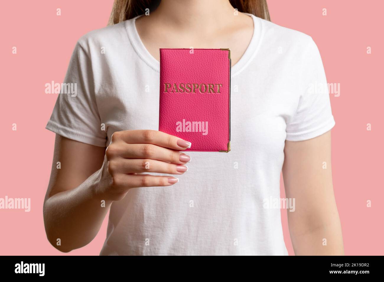 Globale Einwanderung. Aufenthaltserlaubnis. Frau in weißem T-Shirt zeigt Pass in der Abdeckung über verschwommenem Hintergrund isoliert auf rosa. Visa-Zentrum. Rechtsdokum Stockfoto