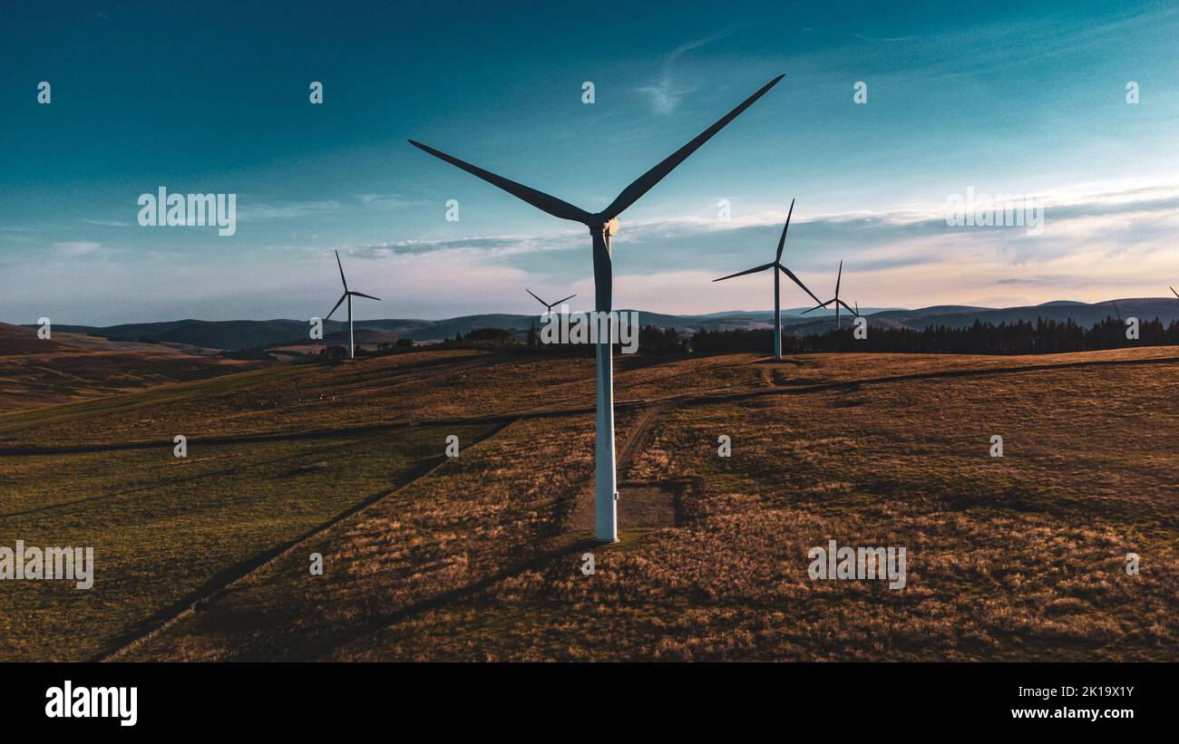 Windpark bei Sonnenuntergang, Stimmung mit Schatten. Wald und Berge im Hintergrund. Das Bild wurde in Scottish Borders, Großbritannien, mit einer Drohne aufgenommen. Stockfoto