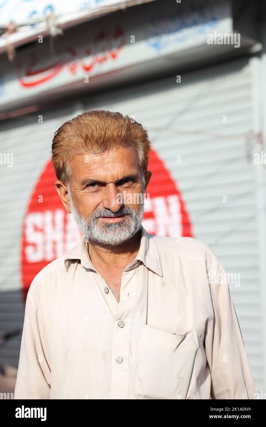 Ein vertikaler, flacher Fokus eines alten pakistanischen Mannes mit einem Bart, der auf der Straße vor einem verschwommenen Hintergrund einer Wand mit Graffiti steht Stockfoto