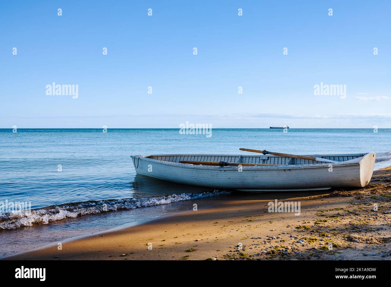 Altes Ruderboot am Strand mit Schatten von Bäumen. Ruhiges Meer am Horizont. Stockfoto