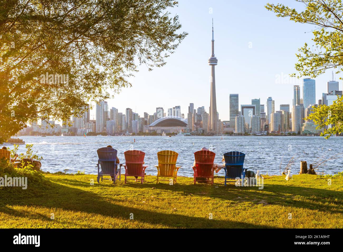 Farbenfrohe Adirondack-Stühle im Toronto Island Park bei Sonnenuntergang. Toronto City Downtown Skyline im Hintergrund. Ontario, Kanada. Stockfoto