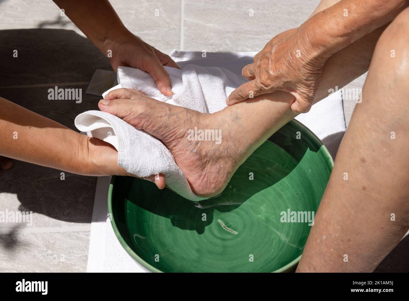 Die weibliche Pflegekraft wischt die Füße der älteren Frau mit einem Handtuch ab. Stockfoto